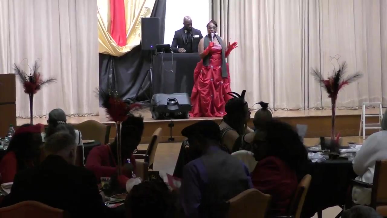 Shant’e Ragin hosting on stage in a red dress before a seated audience